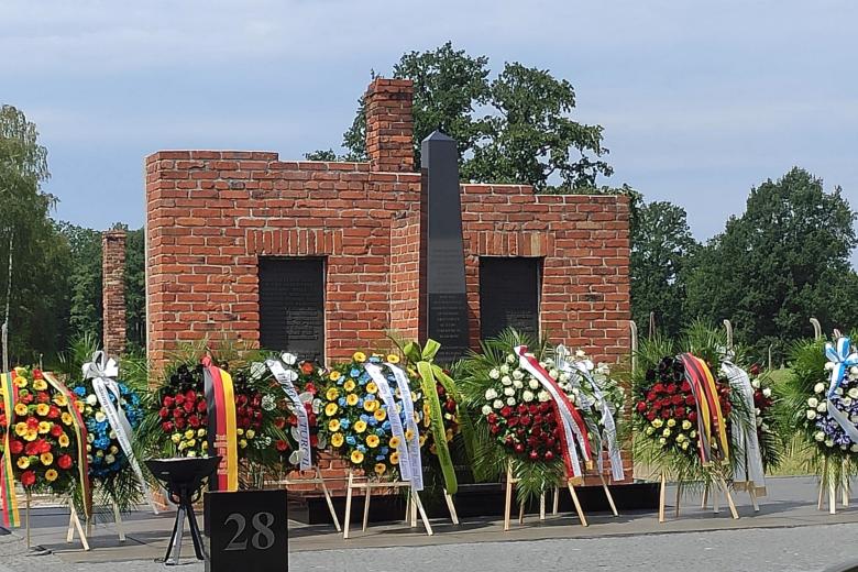 Kilkanaście wieńców kwiatów stojących przy pomniku