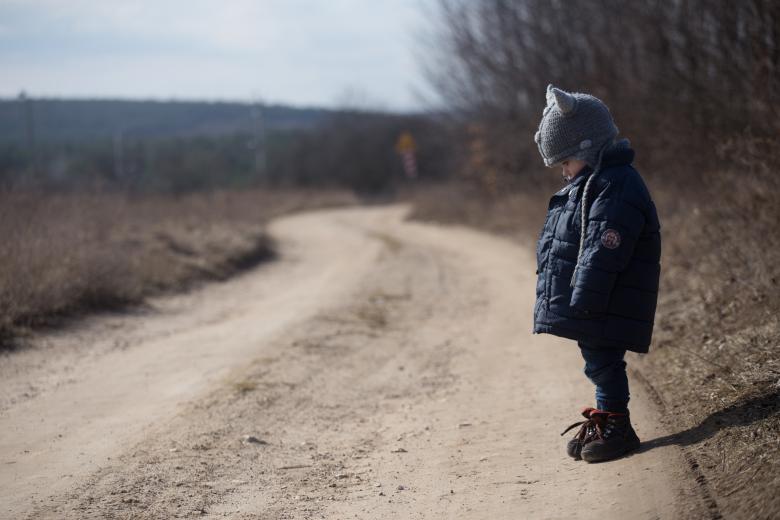 Smutny chłopczyk w kurtce stoi na boku gruntowej drogi z pochyloną głową