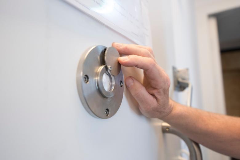 Ręka podnosząca zasłonkę od wizjera w metalowych drzwiach w zakładzie karnym