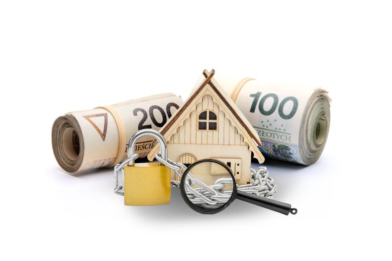 Figurka domu obwiązana zamkniętym na kłódkę łańcuchem. Przed figurką leży lupa, a za figurką zwinięte rulony banknotów sto i dwustuzłotowych