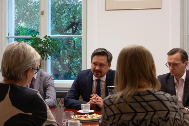 Mężczyzna siedzi przy stole i rozmawia z osobami siedzącymi tyłem po drugiej stronie stołu