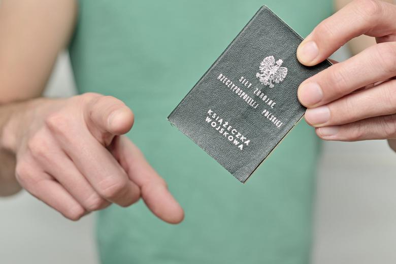 Mężczyzna trzyma książeczkę wojskową i wskazuje palcem do przodu - wskazując jakby osobę oglądającą zdjęcie