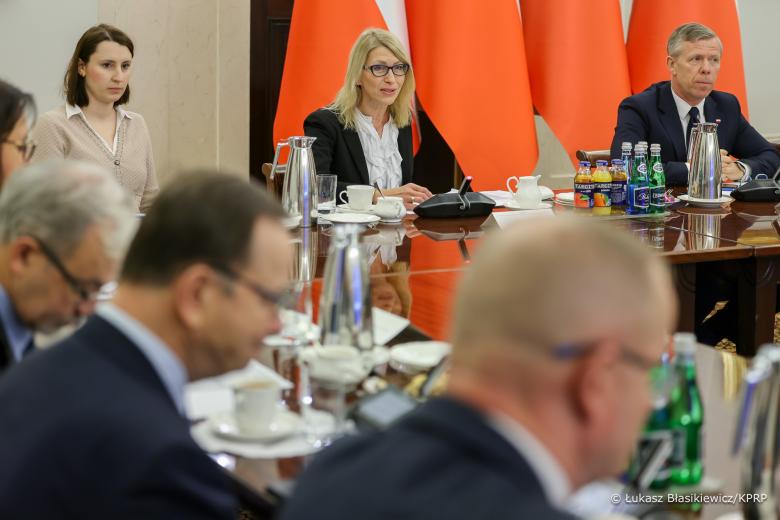 Kilka osób siedzi za podłużnym stołem w sali konferencyjnej