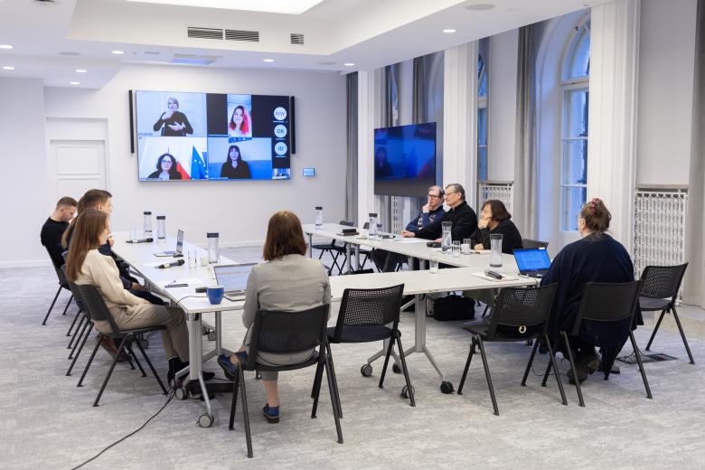 Kilka osób siedzi przy stołach ustawionych w podkowę na sali konferencyjnej