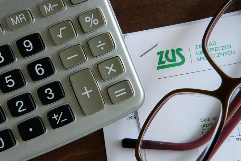 Kalkulator i okluary korekcyjne leżą na dokumencie z logiem Zakładu Ubezpieczeń Społecznych