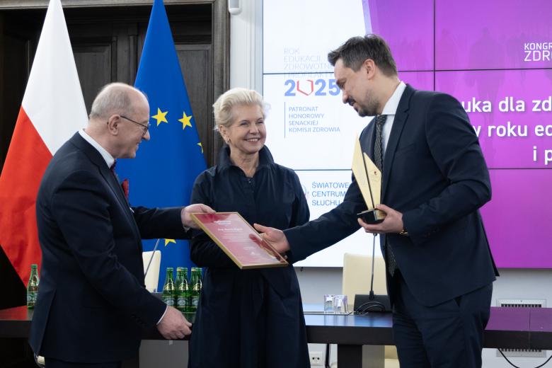 RPO Marcin Wiącek trzymając statuetkę nagrody przyjmuje od Henryka Skarżyńskiego oprawiony dyplom. Pomiędzy nimi stoi uśmiechająca się Beata Małecka-Libera.