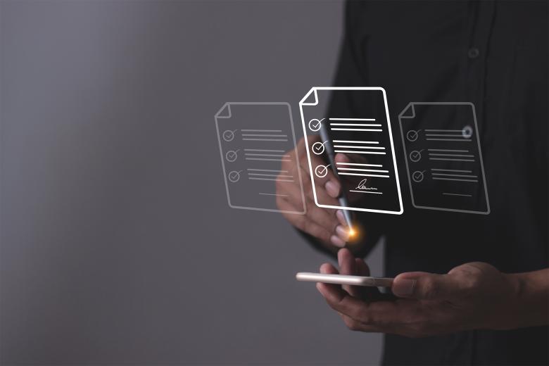 Mężczyzna pracuje na tablecie za pomocą rysiku. Na zdjęcie naniesiona jest ilustracja symbolizująca dokumenty elektroniczne