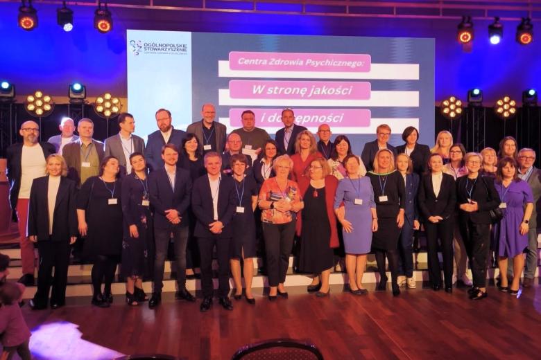 Kilkadziesiąt osób pozuje na stojąco do wspólnego zdjęcia w sali konferencyjnej