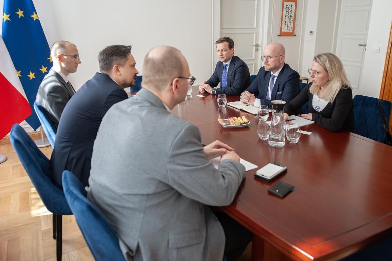 Sześć osób siedzi po dwóch stronach stołu i rozmawia