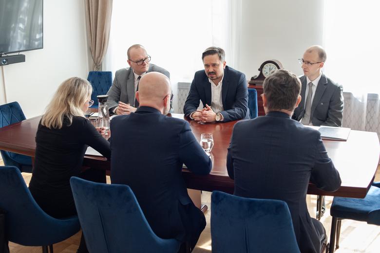 Sześć osób siedzi po dwóch stronach stołu i rozmawia