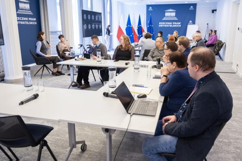 Kilkadziesiąt osób siedzi przy stołach na dużej sali konferencyjnej