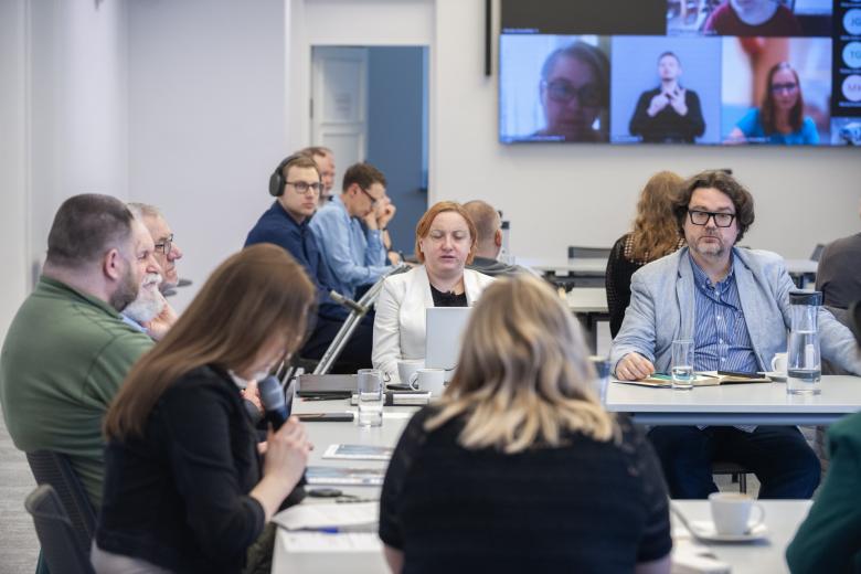 Zbliżenie na osoby siedzące przy stołach na sali konferencyjnej