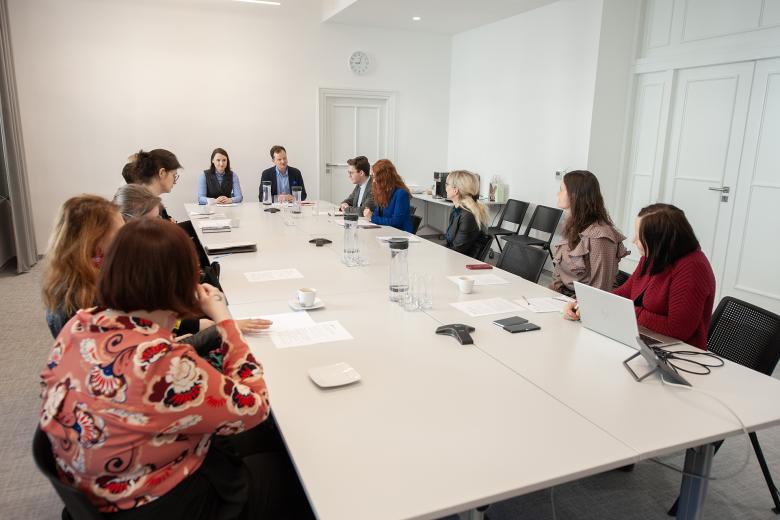 Kilkanaście osób siedzi przy podłużnym stole w sali konferencyjnej