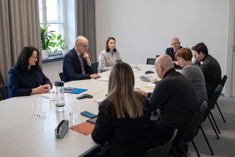 Osiem osób siedzi przy stole w salce konferencyjnej i rozmawia