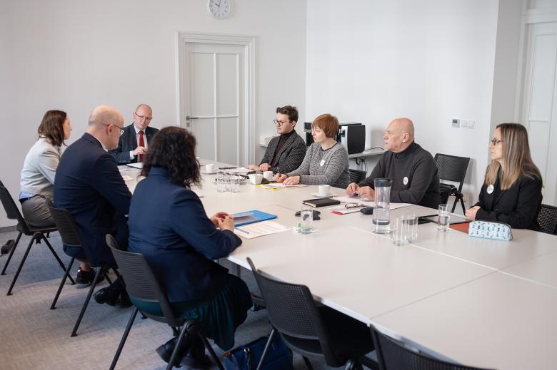 Osiem osób siedzi przy stole w salce konferencyjnej i rozmawia