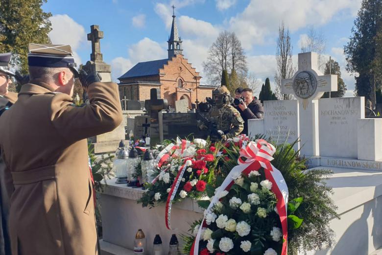Dwie osoby w mundurach salutują przed grobem rodziny Kochanowskich, na którym złożone są wieńce z biało-czerwonymi wstęp