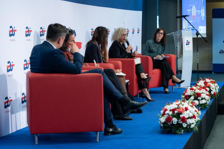 Pięć osób siedzi na fotelach na podwyższeniu w sali konferencyjnej
