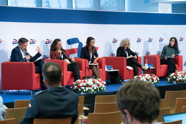 Pięć osób siedzi na fotelach na podwyższeniu w sali konferencyjnej