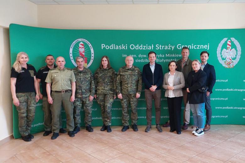 Jedenaście osób, spośród których sześć jest w mundurach, pozuje do zdjęcia na tle ścianki z napisem "Podlaski Oddział Straży Granicznej"