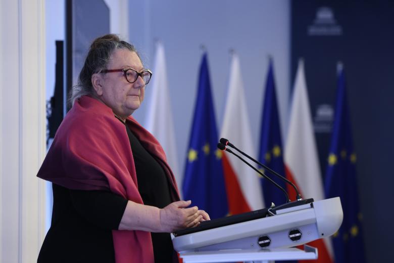 Barbara Imiołczyk wypowiada się do mikrofonu stojąc przy mównicy.