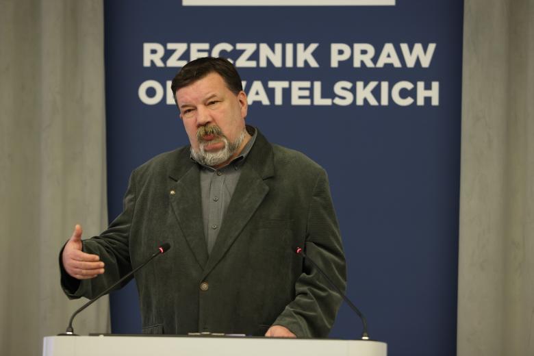 Tomasz Schimanek wypowiada się do mikrofonu stojąc przy mównicy