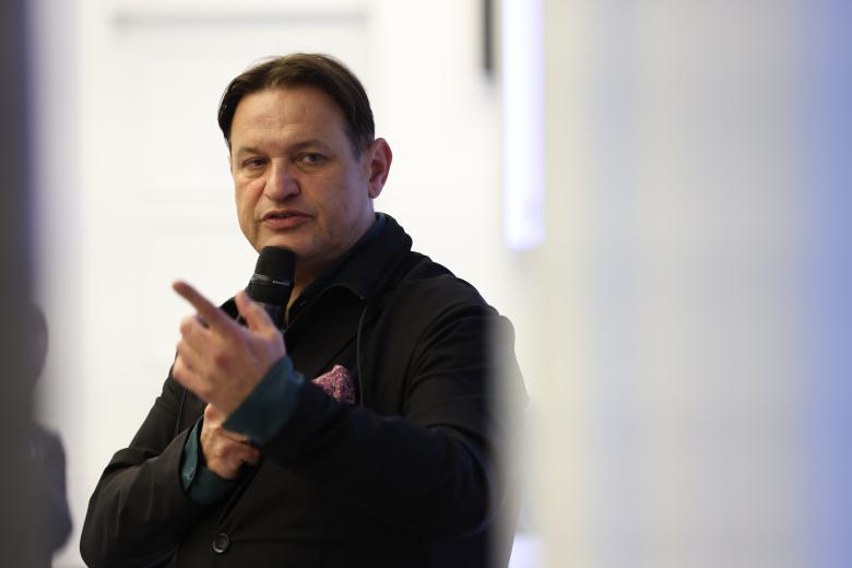 Mężczyzna wypowiada się do trzymanego w dłoni mikrofonu, gestykulując