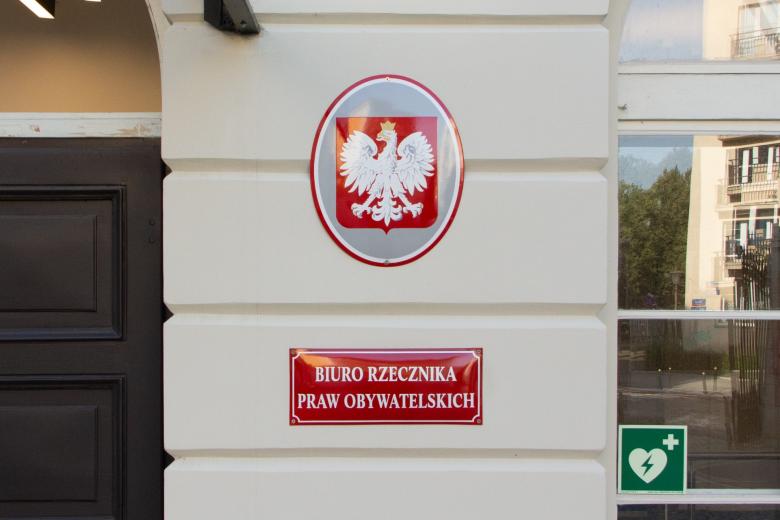 Czerwona tablica z napisem "Biuro Rzecznika Praw Obywatelskich" oraz tablica z polskim godłem narodowym wisząca nad nią