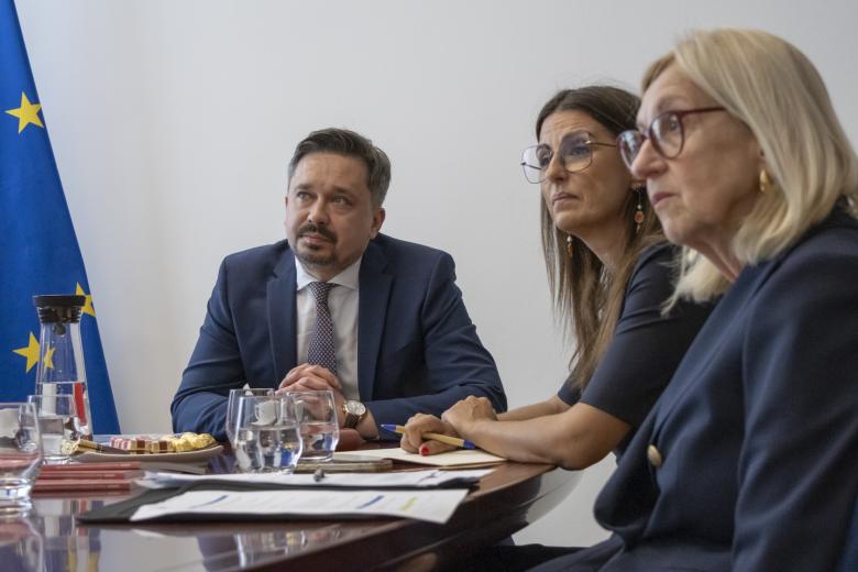 Trzy osoby siedzą przy stole konferencyjnym i patrzą na obiekt znajdujący się poza kadrem