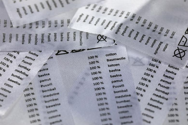 Stos metek, na których w wielu językach zapisana jest informacja o materiałowym składzie artykułu - 100% bawełna