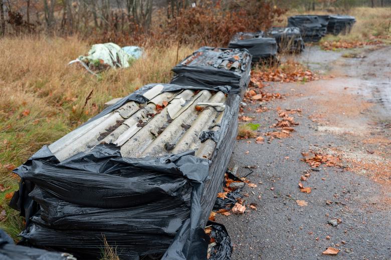 Owinięte folią stosy potłuczonego azbestu stoją na skraju niegospodarowanej polany