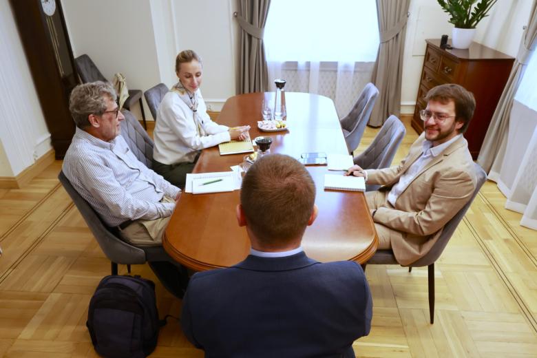 Cztery osoby siedzą przy podłużnym stole i rozmawiają