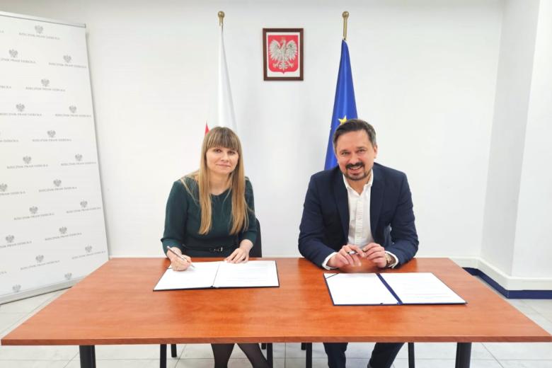 Dwie osoby siedzą za stołem i podpisują dokument