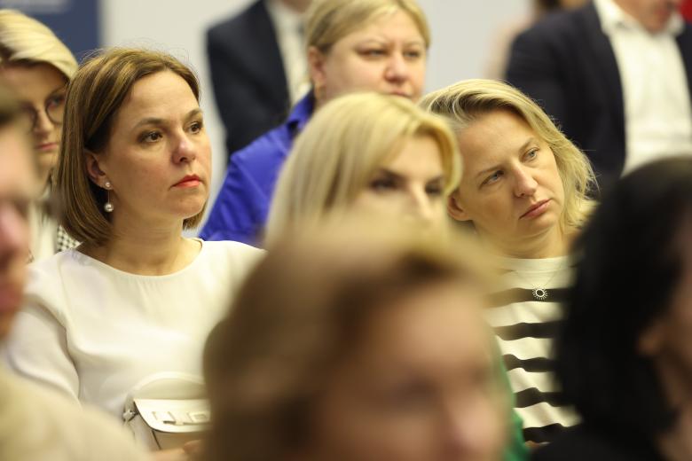 Siedzący w widowni uczestnicy konferencji patrzą w stronę znajdujących się poza kadrem prelegentów