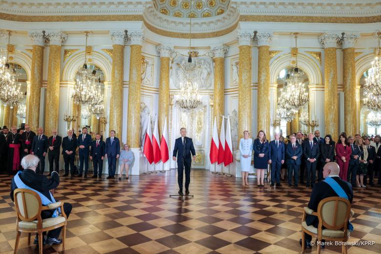 osoba stoi pośrdku sali inni po bokach i przed nią 
