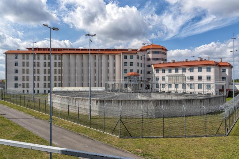 Widok ogólny kompleksu budynków więziennych - wielopiętrowy budynek z kratami w oknach otoczony ogrodzeniem zakończonym drutem kolczastym