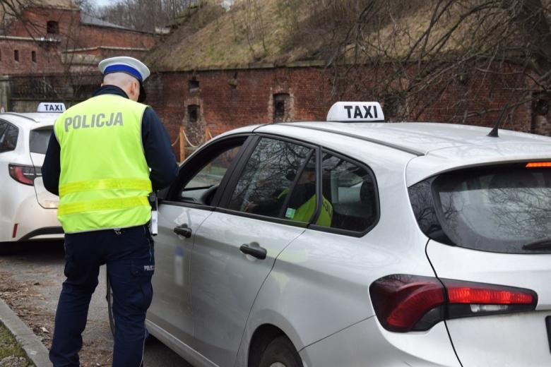 Policjant w mundurze stoi obok samochodu osobowego ze znakiem "TAXI" umieszczonym na dachu.