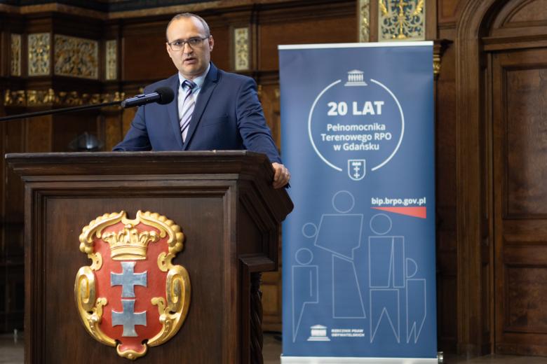 Osoba przemawia za mównicą w zabytkowym, bardzo bogato zdobionym pomieszczeniu w Dworze Artusa w Gdańsku