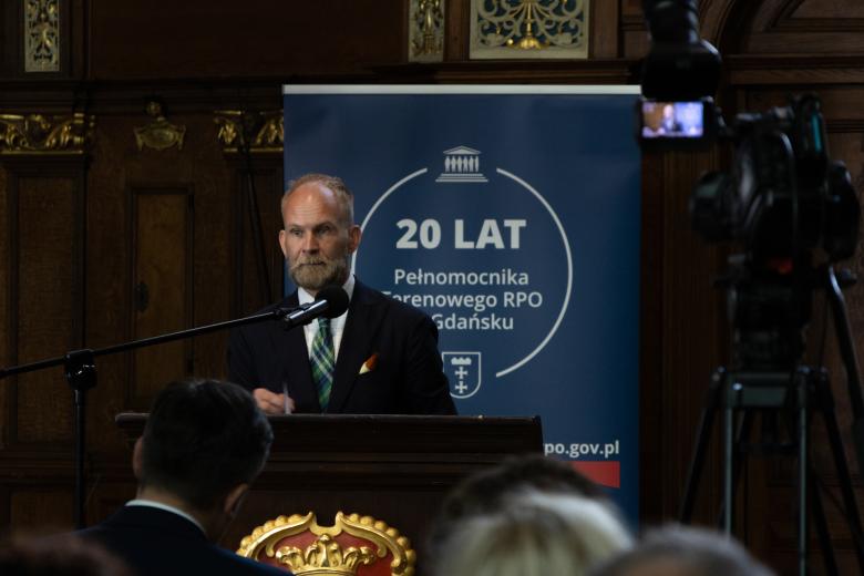 Osoba przemawia za mównicą, w tle granatowy rollup z napisem "20 lat Pełnomocnika Terenowego RPO w Gdańsku"