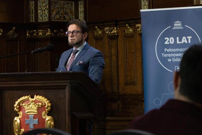 Osoba przemawia za zdobioną, drewnianą mównicą