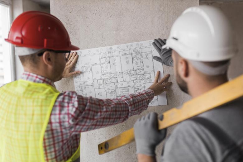 osoby w kaskach na głowach oglądają plan budowlany na ścianie