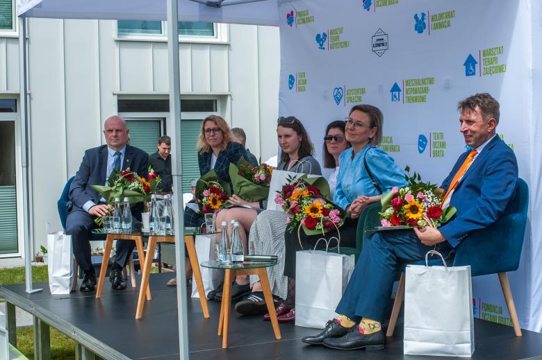 Kilka osób siedzi obok siebie na scenie i trzyma bukiety kwiatów