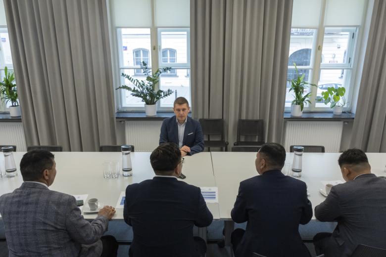 Pięć osób rozmawia siedząc przy stole konferencyjnym. Po jednej stronie stołu siedzi Wojciech Brzozowski, po drugiej - czterech gości.