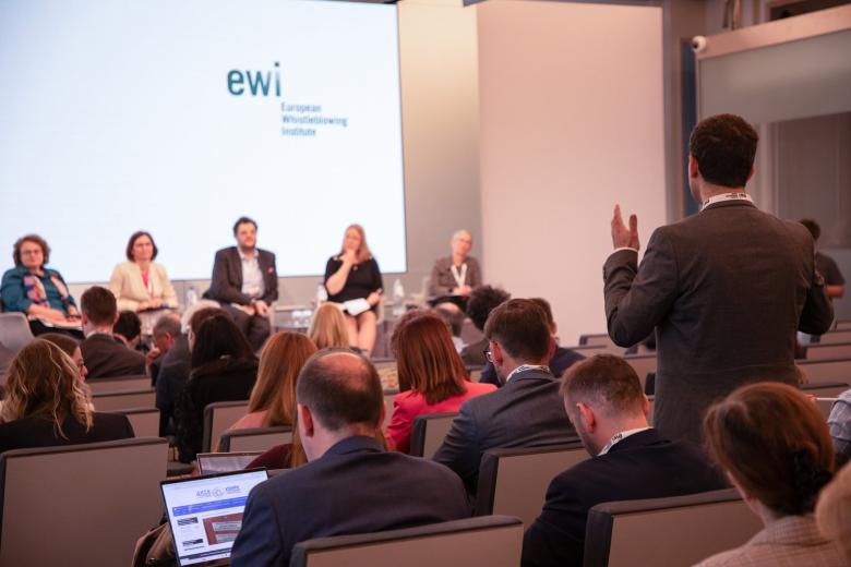 Osoba z widowni stoi i zadaje pytanie osobom siedzącym na przedzie