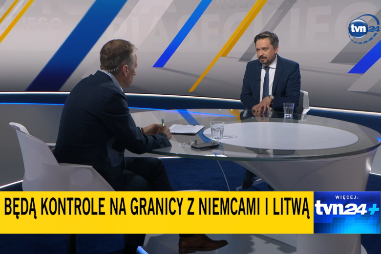 Dwie osoby siedzą w studiu telewizji przy dużym stole