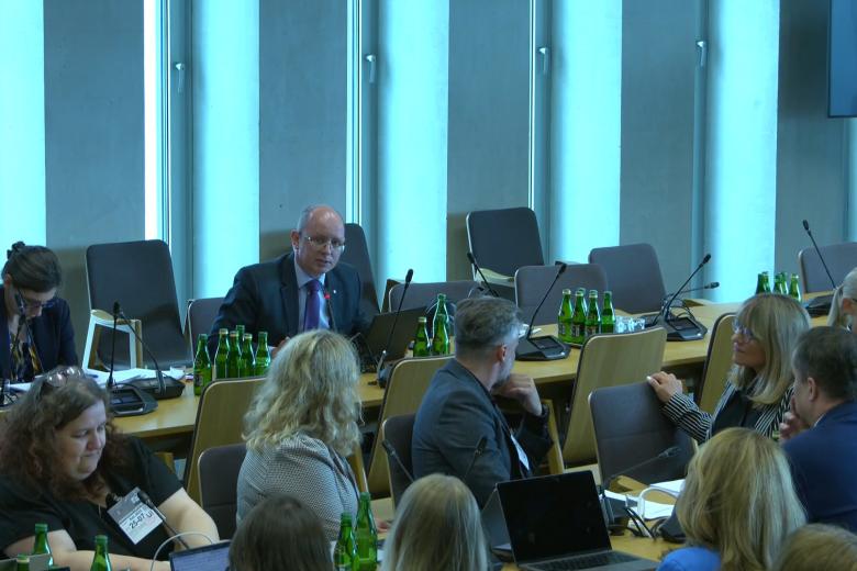 Kilkadziesiąt osób siedzi na sali konferencyjnej słucha osoby, która mówi do mikrofonu