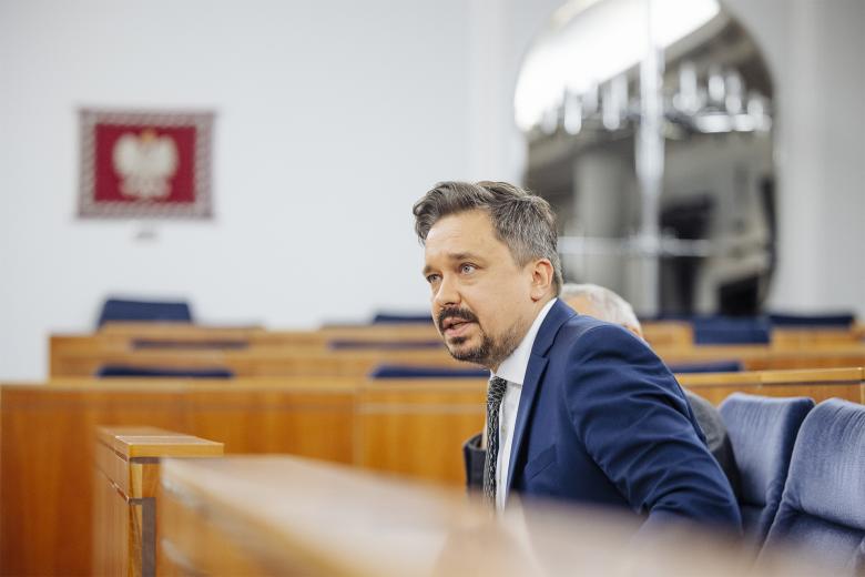 Marcin Wiącek wypowiada się, siedząc w ławie na sali posiedzeń Senatu.