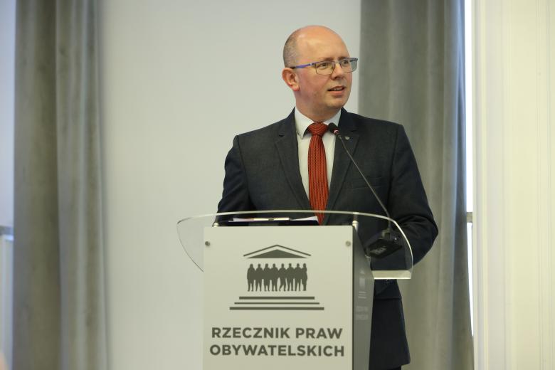 Błażej Kmiecik wypowiada się stojąc przy mównicy