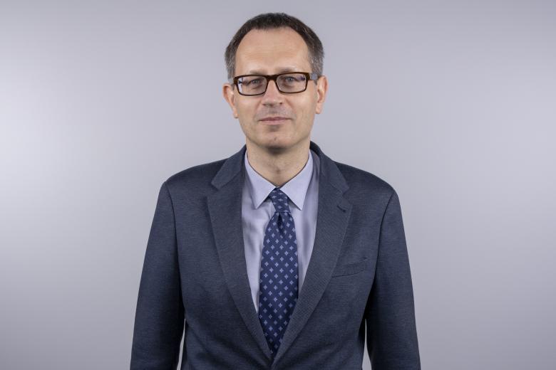 Portret Tomasza Bzukały - lekko uśmiechający się mężczyzna w garniturze i okularach