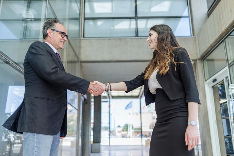 Mężczyzna i kobieta w strojach biznesowych stoją w lobby biurowca i ściskają swoje dłonie