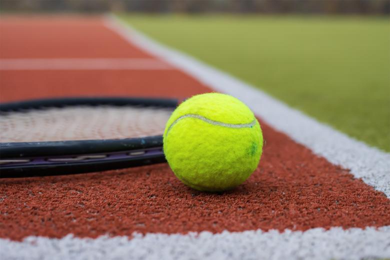 Rakieta i piłka tenisowa leżą na korcie tenisowym